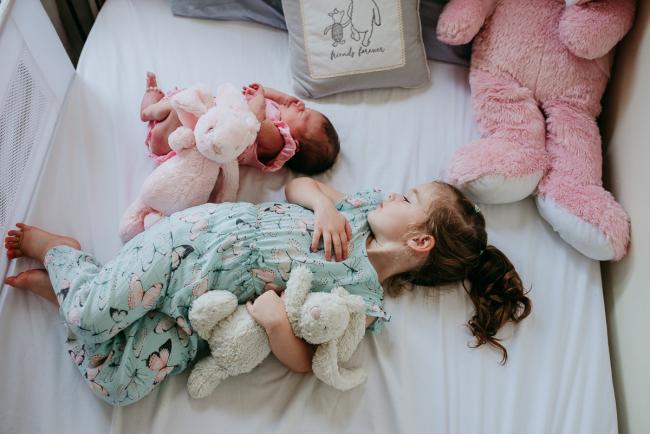 New baby and older sibling lay on a bed next to each other with their bunnies during a Perth newborn lifestyle photography session