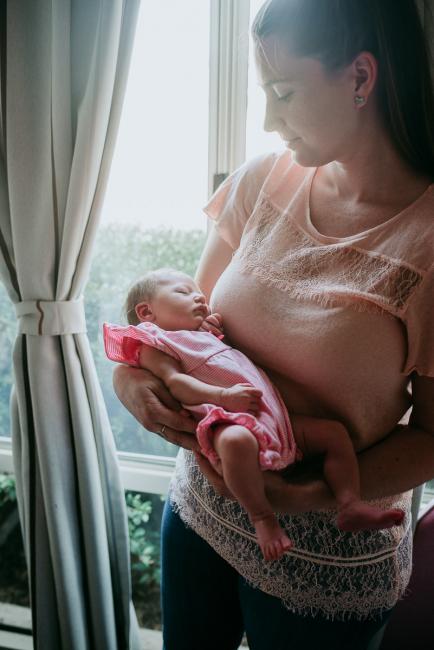 Mother standing by a window and holding her sleeping baby during a Perth newborn lifestyle photography session