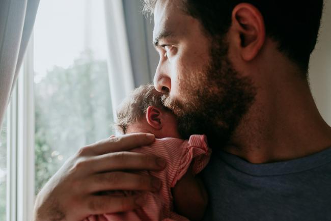 Close up of father kissing his new baby's head as he holds her to his chest during a Perth newborn lifestyle photography session