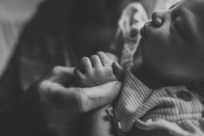Close up black and white image of grandmother holding new baby's hand during a Perth newborn lifestyle photography session