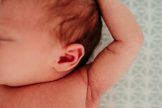 Close up image of a new baby's ear and arm with her arm lifted up as she sleeps during a Perth newborn lifestyle photography session