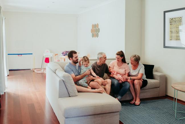 Photo of two kids, two parents, and two grandparents sitting on a couch during a Perth newborn lifestyle photography session