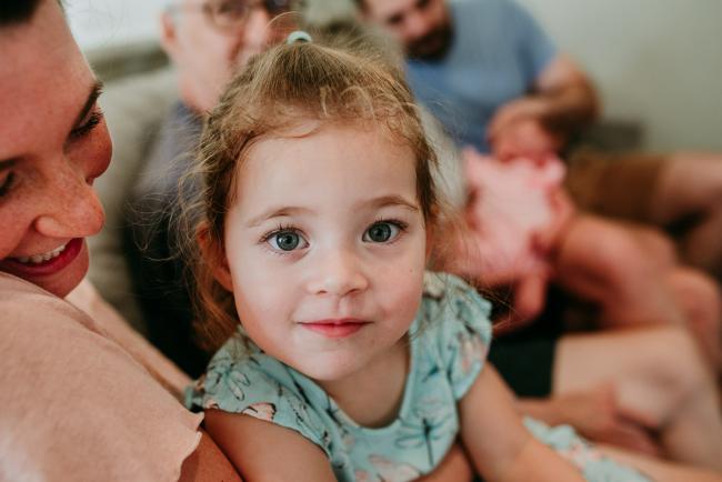 Close up of little girl looking at the camera as she sits on her mum's lap during a Perth newborn lifestyle photography session