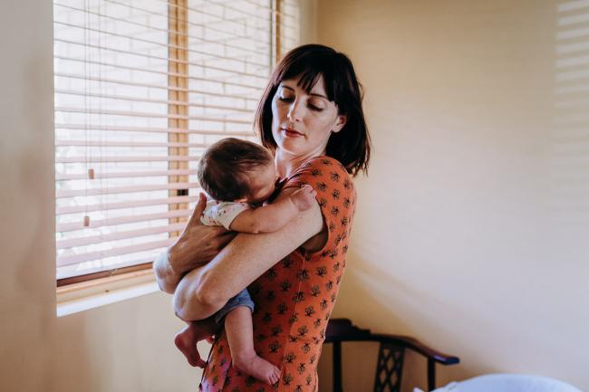 Mother holding her new baby as she looks down at her during a Perth lifestyle Newborn photography session