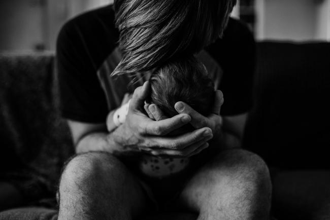 Black and white image of a father holding his new baby's head in his hands and touching their foreheads together during a newborn lifestyle photography Perth session