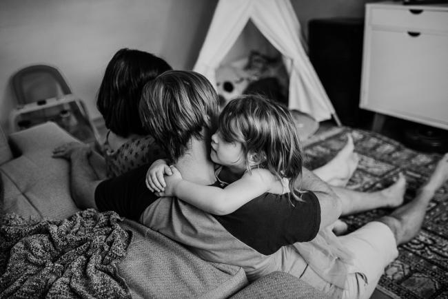 Black and white image of a little girl embracing her father on the couch during a Perth lifestyle Newborn photography session