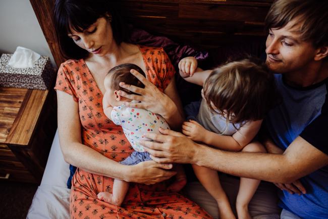 New baby lays on mums chest as dad and sister reach over to touch her during a Perth lifestyle Newborn photography session