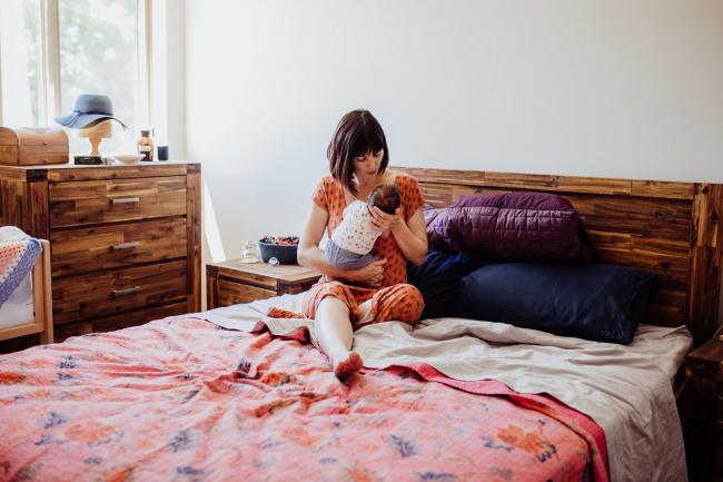 Mother sits on the bed holding her new baby during a Perth lifestyle Newborn photography session