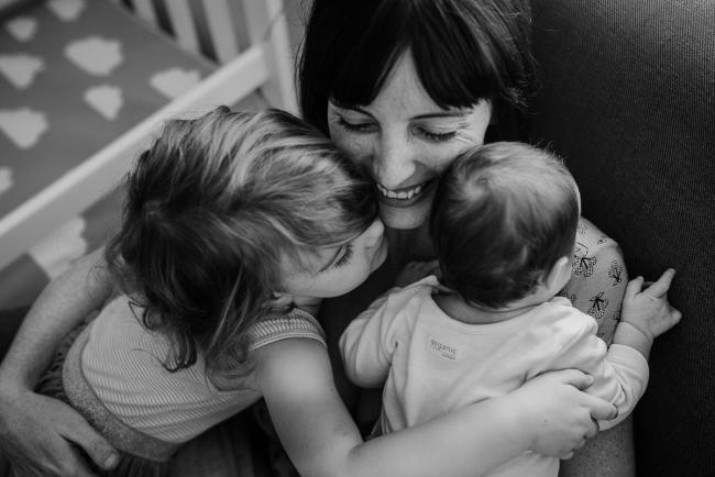 black and white image of mother holding her new baby and her toddler daughter in her arms during a newborn lifestyle photography Perth session