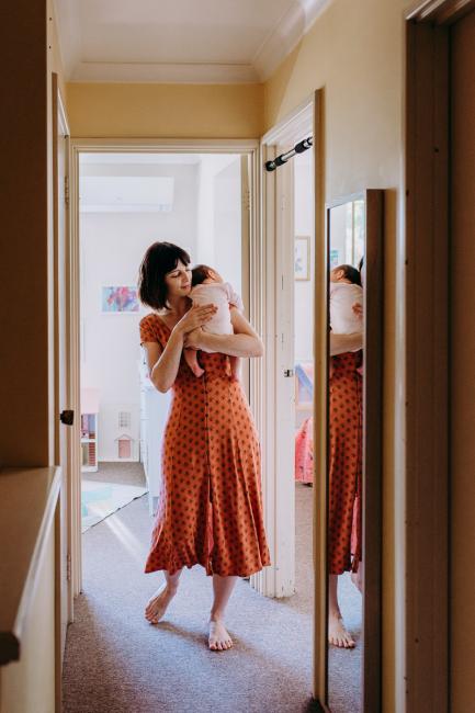 Mother holding her new baby over her shoulder as she walks down the hallway during a Perth lifestyle Newborn photography session