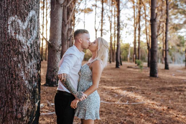 Perth-Couples-Photography-15-of-27 Couple holding hands and kissing next to a tree with a love heart on it at The Pines Wanneroo during a Golden Hour Perth couples photography session