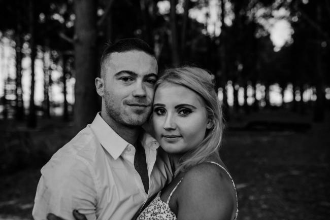 Perth-Couples-Photography-19-of-27 Black and white image of a couple looking at the camera with thier heads next to each other at The Pines Wanneroo during a Golden Hour Perth couples photography session