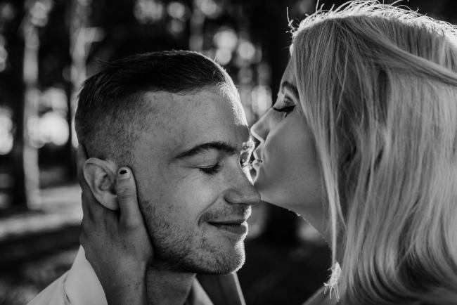 Black and white close up image of woman kissing her partner while he closes his eyes and smiles during a Perth couples photography session at The Pines in Wanneroo