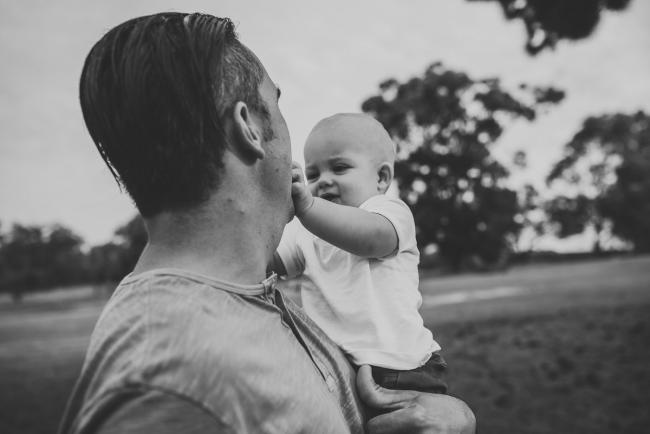 Black and white image of father holding his son who is touching his face during a Perth extended family photography session