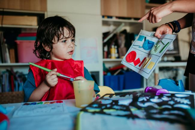 Perth-Family-Photographer-15-of-26 Little boy painting while wearing a red art smock and looking at a drawing with Perth family photographer