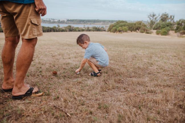 Little boy squatting down and playing with a golf ball during a Perth extended family photography session