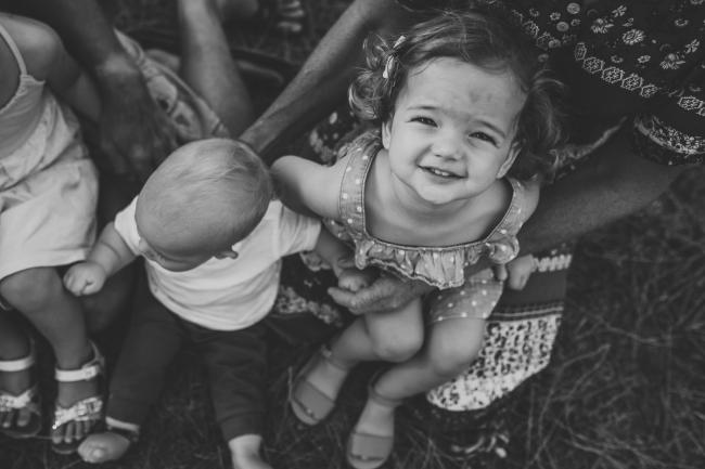 Black and white top down image of a little girl sitting on her grandmothers lap next to her baby cousin during a Perth extended family photography session