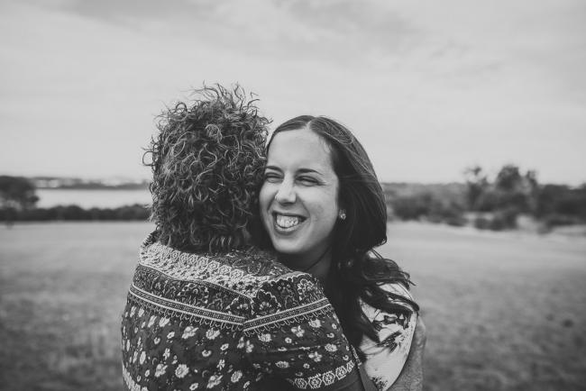 Black and white image of an older daughter looking over her mother's shoulder as they hug during a Perth extended family photography session