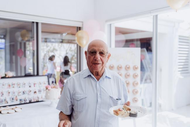 Nonno standing in front of party decorations holding his plate of food during a birthday party captured by Perth events photographer