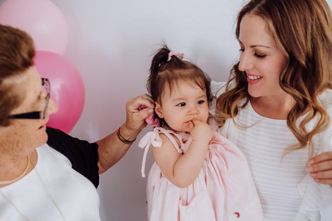 Nonna playing with the hair of her granddaughter who is being held by her mother during a birthday party captured by Perth events photographer