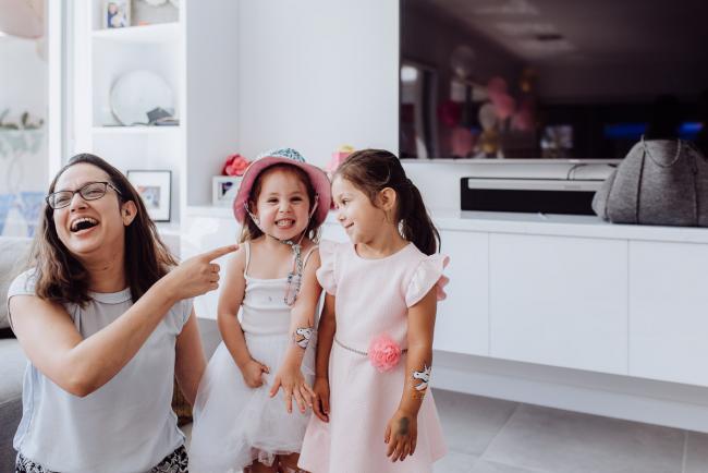 Woman laughing and pointing at two girls who are smiling during a birthday party captured by Perth events photographer