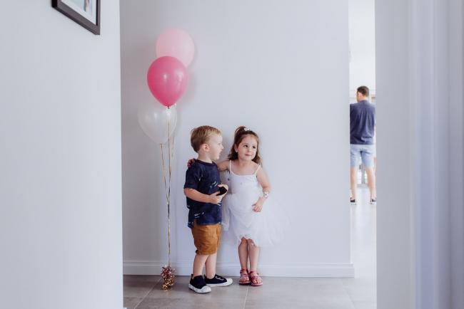 Little boy and girl standing next to each other and two pink balloons during a birthday party captured by Perth events photographer