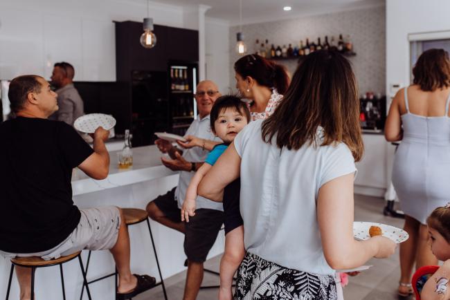 Little boy looking over the shoulder of his mother in a crowded room during a birthday party captured by Perth events photographer