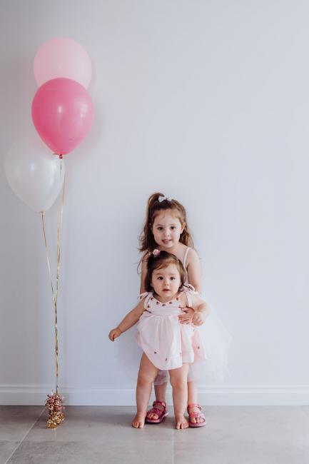 Two little girls standing next to two pink balloons during a birthday party captured by Perth events photographer