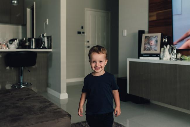 Little boy smiling at the camera in the middle of his living room during a Perth lifestyle newborn photography session