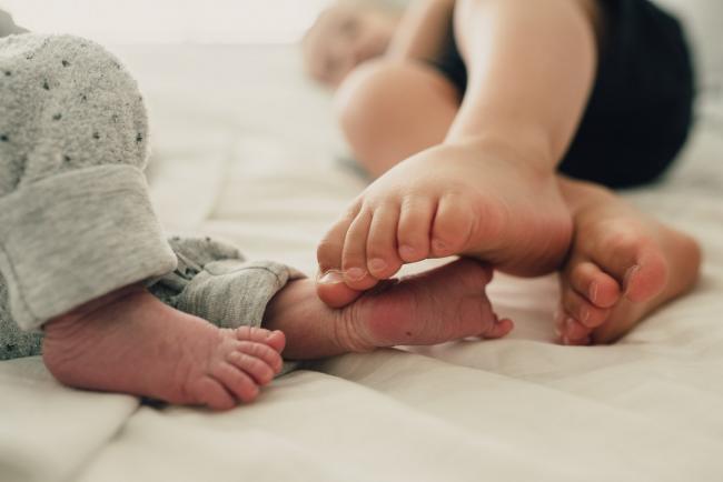 New baby feet and toddler feet touching each other during a lifestyle newborn photography Perth session