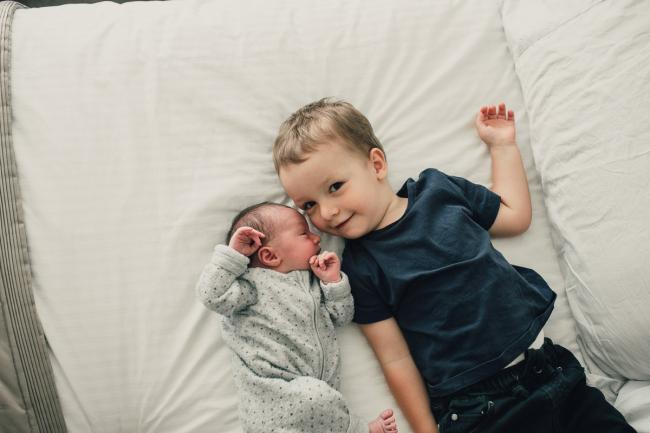 Little boy laying on the bed next to his new baby sister during a Perth lifestyle newborn photography session