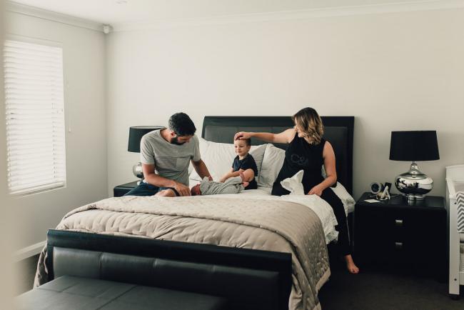 New baby on the bed as dad looks down at her and mum touches brothers head during a Perth lifestyle newborn photography session