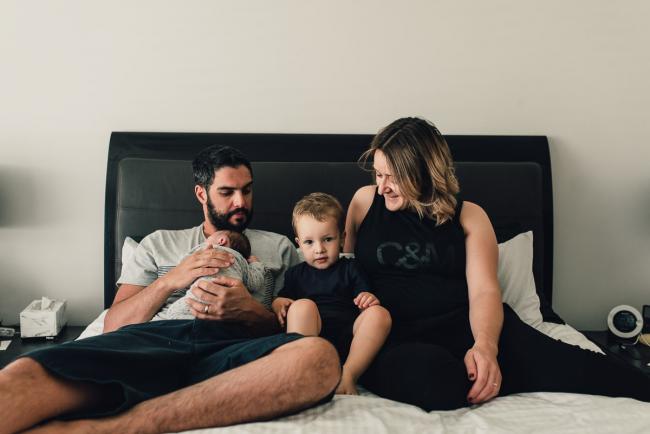 Family of 4 sitting on a bed during a Perth lifestyle newborn photography session