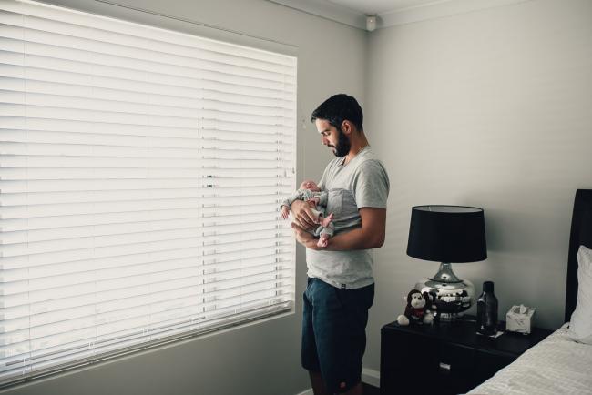 Dad standing by the window holding his new baby during a lifestyle newborn photography Perth session