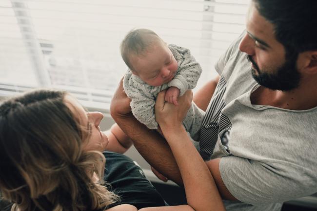 Father passing new baby to mother during a Perth lifestyle newborn photography session