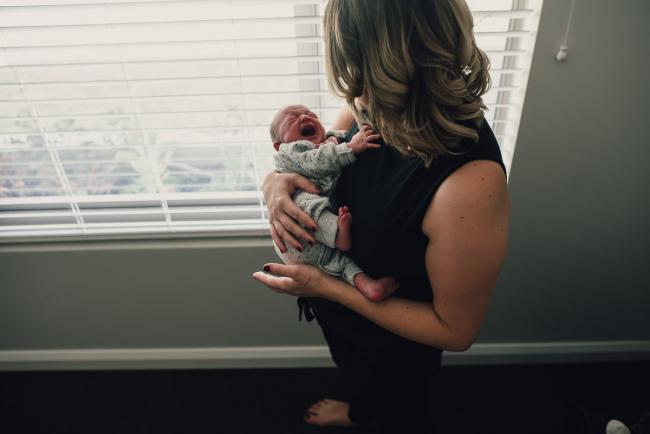 Mother holding her new baby as the baby cries during a Perth lifestyle newborn photography session