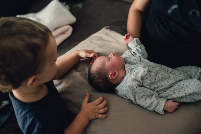 Little boy touching the head of his new babu sister as she lays on a pillow during a Perth lifestyle newborn photography session