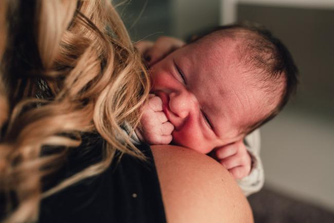 New baby with her fingers in her mouth as she looks over mums shoulder during a Perth lifestyle newborn photography session