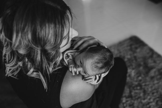 Top down black and white image of new baby being held on the shoulder of her mother during a Perth lifestyle newborn photography session