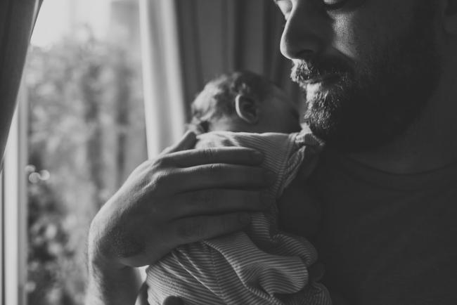 Black and white close up image of a father holding his new baby to his chest during a Perth newborn lifestyle photography session