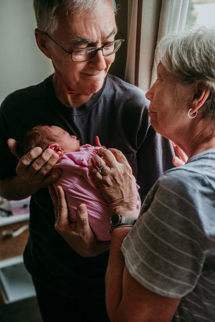 Grandparents smiling at each other as they hold their new baby granddaughter during a Perth newborn lifestyle photography session