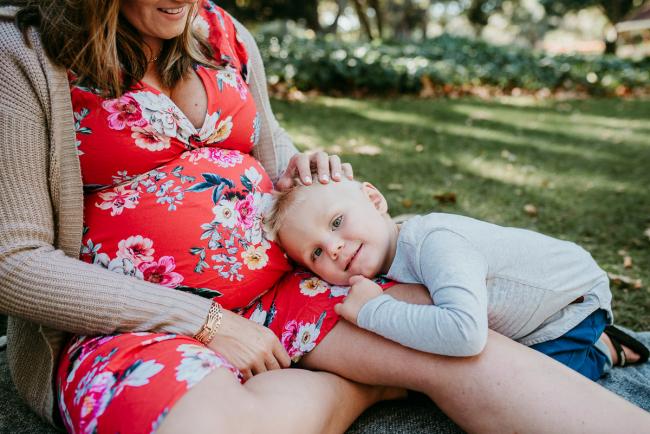 Little boy laying across the lap of his pregnant mother as she strokes his hair during a Perth maternity session at Hyde Park