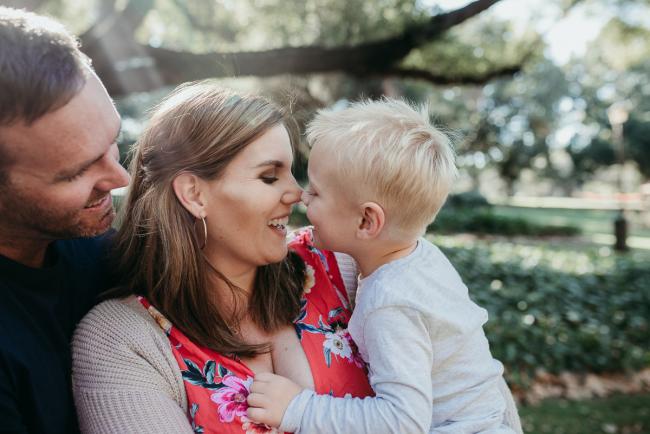 Dad smiling at his wife and son who are touching noses and smiling during a Perth maternity session at Hyde Park