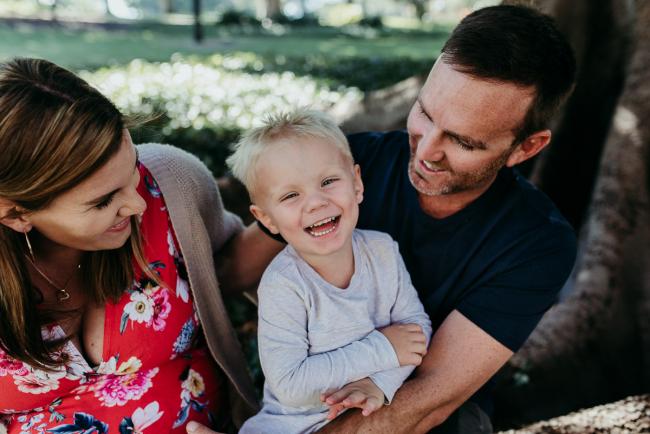 Little boy laughing as he's being held by his mother and father during a Perth maternity session at Hyde Park