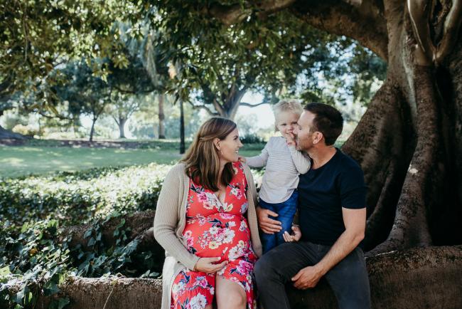 Pregnant woman sitting on a tree branch next to her husband and little boy during a Perth maternity session at Hyde Park