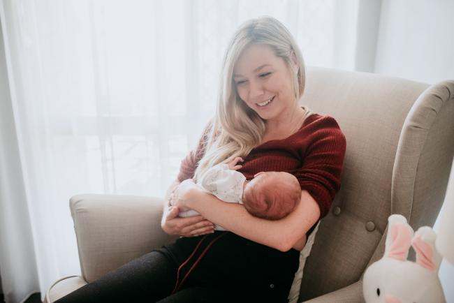 Newborn-Photographer-Perth-11-of-37 Mother holding her new baby in a feeding chair and smiling during a Perth newborn lifestyle session