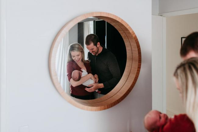 Looking into a mirror as parents hold their new baby during a Perth newborn lifestyle session