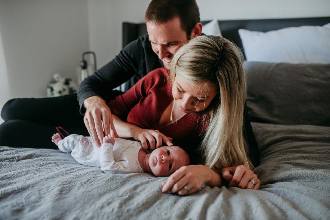 Newborn-Photographer-Perth-21-of-37 Mum and dad laying on the bed and looking at their newborn baby during a Perth newborn lifestyle session