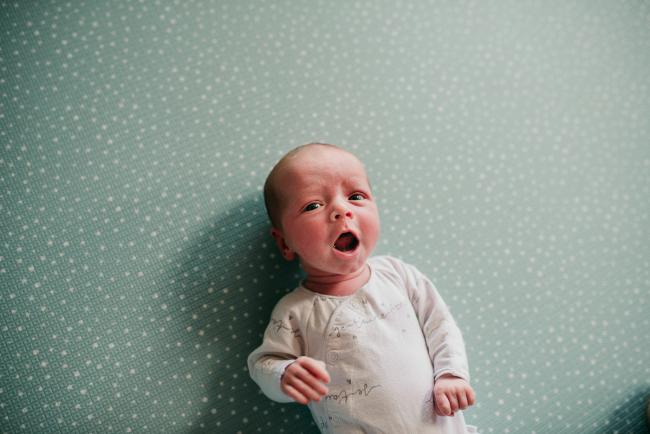 Newborn-Photographer-Perth-23-of-37 Newborn baby yawning as she lays on a green spotty mat during a Perth newborn lifestyle session