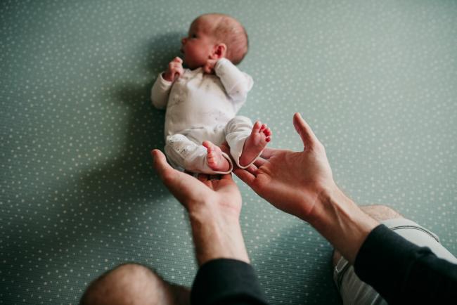 Newborn-Photographer-Perth-24-of-37 Father holding the feet of his newborn baby as she lays on a green mat during a Perth newborn lifestyle session